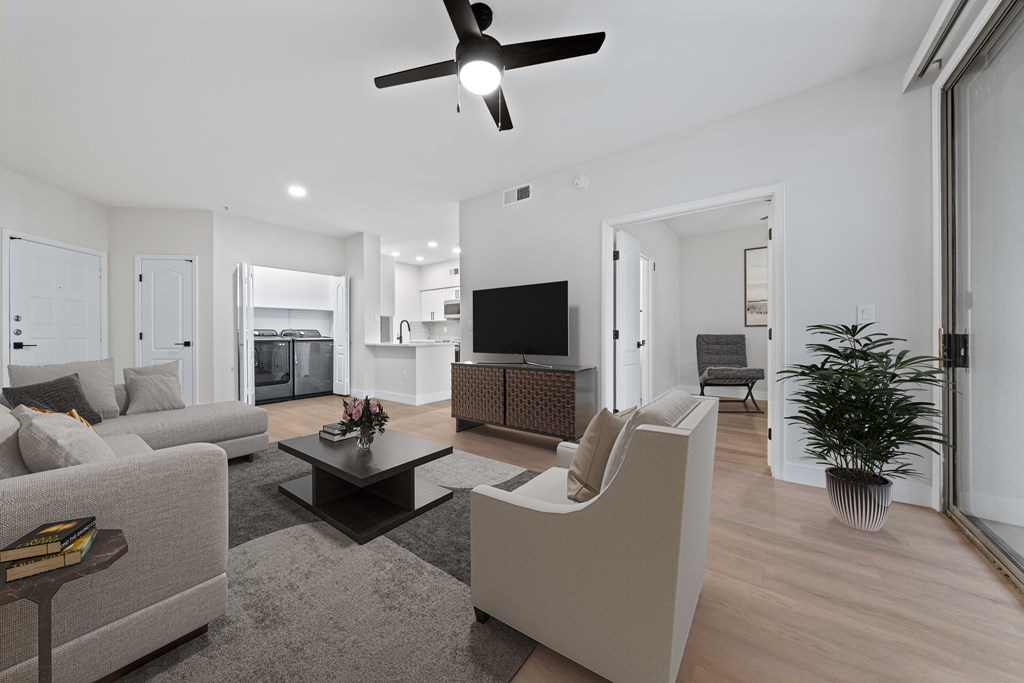 a living room with couches and a kitchen and a ceiling fan